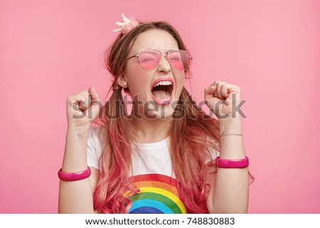 Portrait of excited overjoyed female model clenches fists with pleasure, screams in happiness, celebrates her victory, has great triumph. Fashionable woman gestures joyfully indoors. Success concept