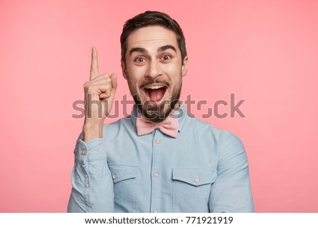 Studio shot of intelligent bearded man raises fore finger as recieves good idea or glad find out about successfully passed exam. Excited cheerful man remembers something pleasant, isolated on pink