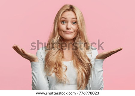 Pretty blonde female with blue eyes and blonde hair, shrugs shoulders, being doubtful about making serious decision, feels uncertain, isolated over pink background. Hesitation and confusion. Foto stock © 