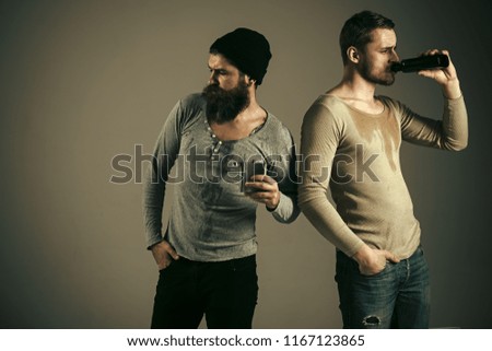 Alcohol, addiction, leisure. Guys hold bottle and flask with alcohol, drinking. Company of dirty sweaty friends spend leisure with drinks. Men on drunk faces, grey background. Alcohol addict concept.
