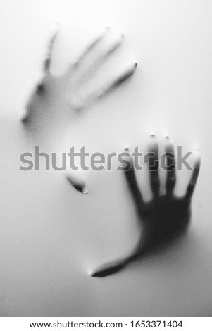 A vertical greyscale shot of a person's hands behind a frozen glass - fear and bad dreams concept
