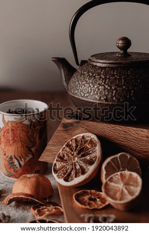 A vertical shot of a cup of tea with teapot and dry lemon slices
