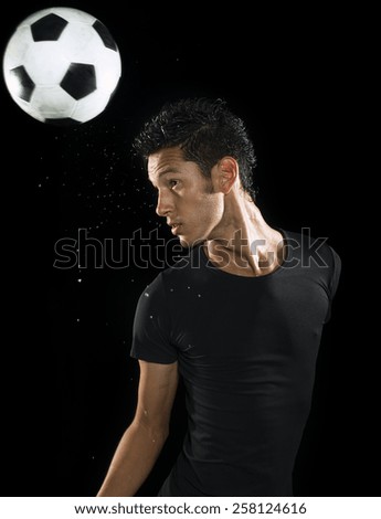 A young sweaty soccer player sweating on a low key setting with soccer ball.