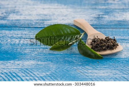 Tea and dried tea in wooden spoon to right on a wooden blue and white. Focus dark tea leaves.