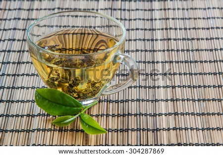 Tea and fresh tea leaves on the floor bamboo. Focus on the tea leaves and glass.