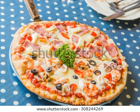 Hawaiian Pizza and Seafood In white plate placed on a blue and white striped fabric. The background is blurred and poor light.