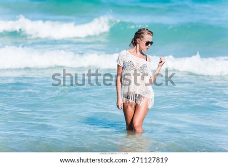 sexy girl in a black bikini and a white ?ape and sunglasses walks along the beach near the sea