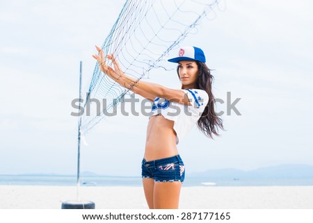 sports sexy brunette in denim shorts and a short t-shirt posing on the volleyball court with net and ball