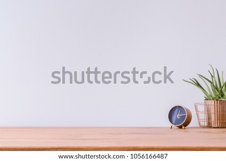 Foto de mesa de escritório em casa de madeira com relógio preto e dourado e planta verde fresca contra parede vazia branca