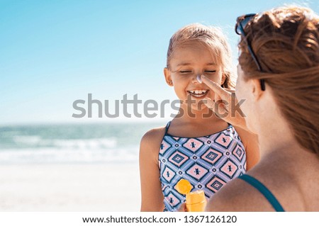 Mãe jovem aplicando protetor solar protetor no nariz da filha na praia. Mulher mão colocando loção solar no rosto da criança. Menina bonita com protetor solar à beira-mar com espaço de cópia.