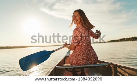 Smiling young woman looking back over her shoulder while paddling a canoe on a lake on a sunny summer afternoon