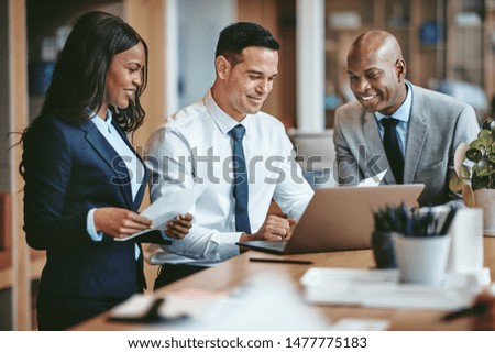 Smiling group of diverse businesspeople going over paperwork together and working on a laptop at a table in an office