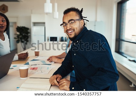 Young African American business professional smiling while sitting with a group of colleagues during a meeting in an office