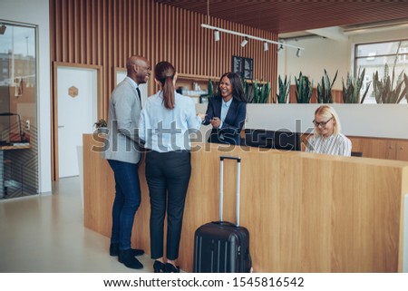 Two smiling guests talking to a concierge while checking in together at the reception counter of a hotel