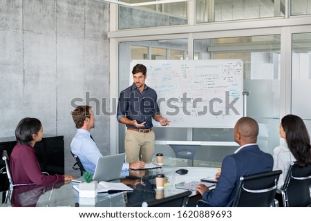 Executivo da empresa apresentando nova estratégia de gestão para a equipe na sala de conferências. Homem de negócios bem sucedido dando relatórios aos seus colegas. Jovem gerente apresentando no quadro branco seus planos de negócios.