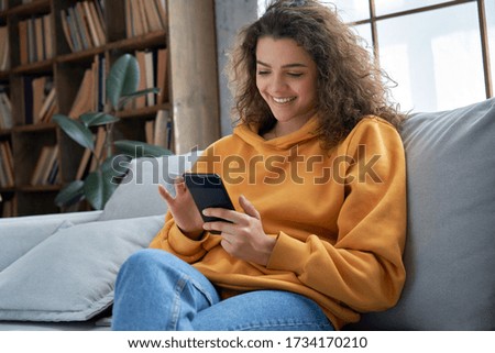 Happy millennial hispanic teen girl checking social media holding smartphone at home. Smiling young latin woman using mobile phone app playing game, shopping online, ordering delivery relax on sofa. Сток-фото © 