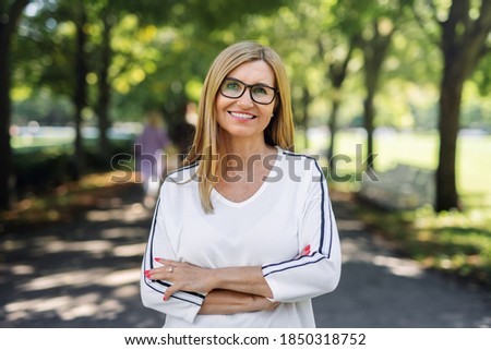 Happy senior woman looking at camera outdoors in city or town park.