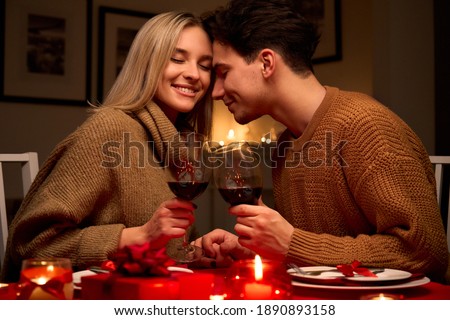 Feliz pareja de jóvenes enamorados que se aferran a las copas bebiendo vino tinto teniendo una cena romántica en la noche de San Valentín o disfrutando del aniversario sentados en la mesa en casa o en el restaurante.