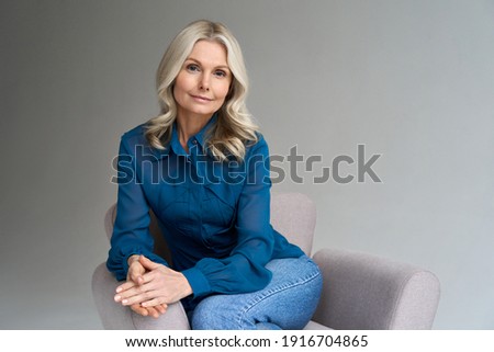 Middle aged female psychotherapist, counselor sitting in chair alone in office looking at camera. Sophisticated elegant mature 50s woman of mid age with blond hair posing indoors, portrait. Stockfoto © 