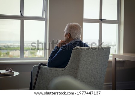 Rear view of senior man sitting on armchair and looking through the window. Lonely old man sitting at home near window during covid19 outbreak. Thoughtful retired man abandoned at nursing home. Foto stock © 
