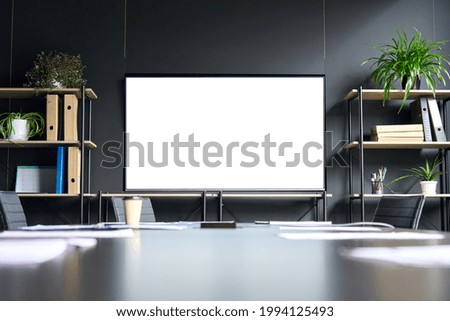 Sala de reuniones con monitor de pantalla en blanco vacío de maquillaje en tv para publicidad en oficina contemporánea moderna sobre fondo de pared negra. No hay gente. Concepto de tecnologías empresariales.