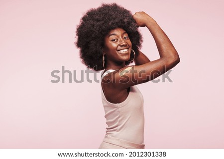 Smiling young African woman flexing her arm with a bandage on it after a Covid vaccination against a pink background