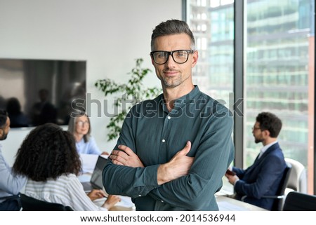 Smiling confident mature businessman leader looking at camera standing in office at team meeting. Male corporate leader ceo executive manager wearing glasses posing for business portrait arms folded. Stock foto © 