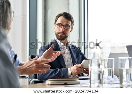 Serious Caucasian bearded male ceo wearing glasses looking at female manager controlling discussing corporation project report at table. Executive managers leaders working together in modern office. 商業照片 © 