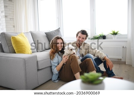 Feliz pareja joven enamorada de un perro sentado en casa, mirando la cámara.
