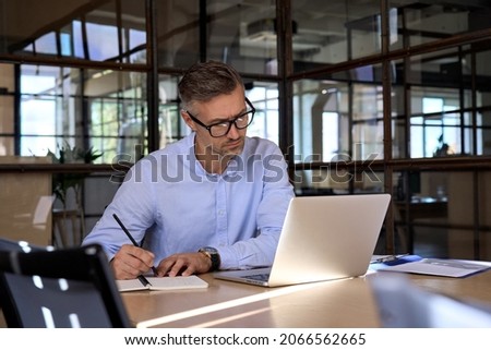 Mature business man executive manager looking at laptop computer watching online webinar training or having virtual meeting video conference taking notes, doing market research working in office. Foto stock © 