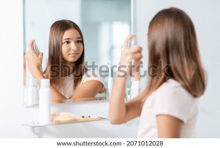concepto de belleza y de personas - adolescente que busca espejo y usa aerosol de estilo en el baño de su casa
