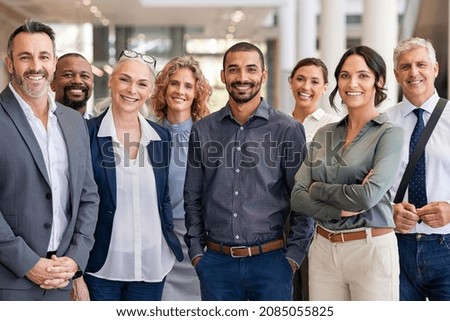 Photo of Portrait of successful group of business people at modern office looking at camera. Portrait of happy businessmen and satisfied businesswomen standing as a team. Multiethnic group of people smiling.