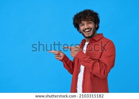 Happy excited young indian man looking at camera pointing aside with fingers hand gesture at copy space advertising new promotion, presenting sale offer standing isolated on blue background. ストックフォト © 