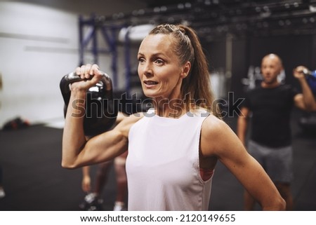 Fit mature woman in sportswear lifting a dumbbell during a strength training session at the gym
