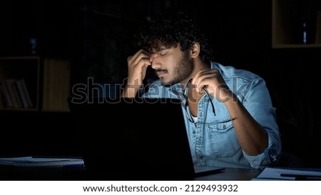 Overworked young indian businessman taking off glasses working late at night. Tired sleepy stressed student holding eyeglasses feeling lack of sleep, having eyestrain problem, using laptop computer. Stock foto © 