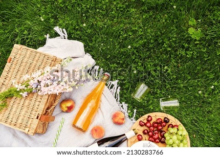 leisure and drinks concept - close up of food, drinks and basket on picnic blanket on grass