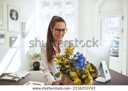 Smiling young female architect wearing glasses standing in her office holding a bouquet of freshly cut flowers