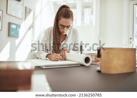 Young female architect sitting in an office drawing in a sketchbook and working with a scale model 