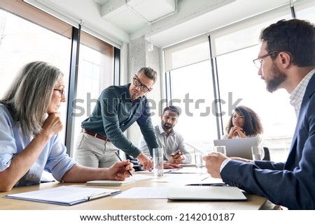 Photo of Male mature caucasian ceo businessman leader with diverse coworkers team, executive managers group at meeting. Multicultural professional businesspeople working together on research plan in boardroom.