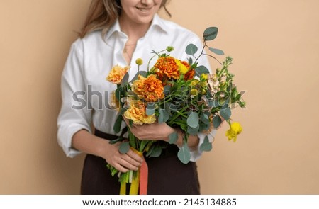 people and floral design concept - close up of smiling woman with bunch of flowers over beige background
