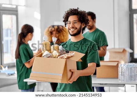 charity, donation and volunteering concept - happy smiling male volunteer with food in box and international group of people at distribution or refugee assistance center Foto d'archivio © 