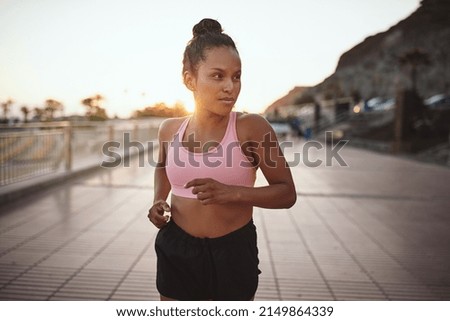 Fit young African woman in a halter top and shorts jogging alone along a promenade early in the morning