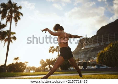Young African woman in a tank top and shorts practising yoga alone in a city park on a sunny summer afternoon