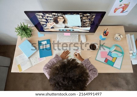 Table top view of African American teen pupil writing learning with teacher's tutor's video class on desktop computer at home. Remote distant homeschooling concept. Photo stock © 