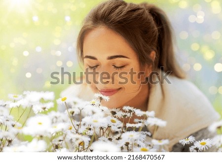 gardening and people concept - close up of happy young woman smelling chamomile flowers at summer garden