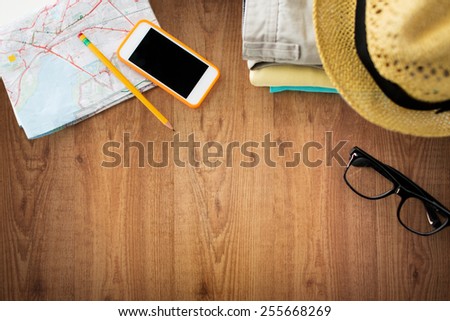 concepto de viajes, vacaciones de verano, turismo y objetos - cierre de ropa plegada, smartphone y mapa turístico sobre mesa de madera