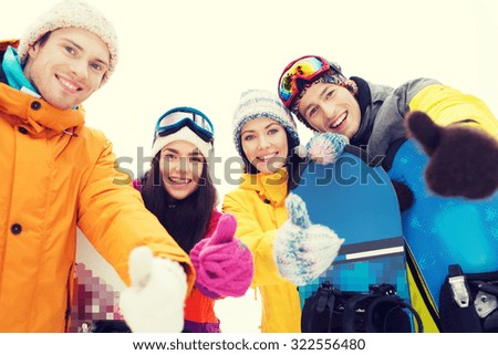 winter, leisure, extreme sport, friendship and people concept - happy friends with snowboards showing thumbs up