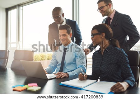 Group of happy diverse male and female business people in formal gathered around laptop computer in bright office