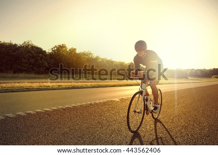 Un solo ciclista con pantalones cortos, casco y gafas de sol entrenando para carreras de larga distancia en bicicleta por carretera al amanecer con espacio de fotocopias delante