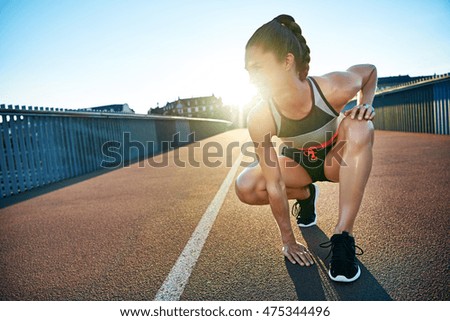 Sun highlights kneeling female jogger as she places one hand on the pavement